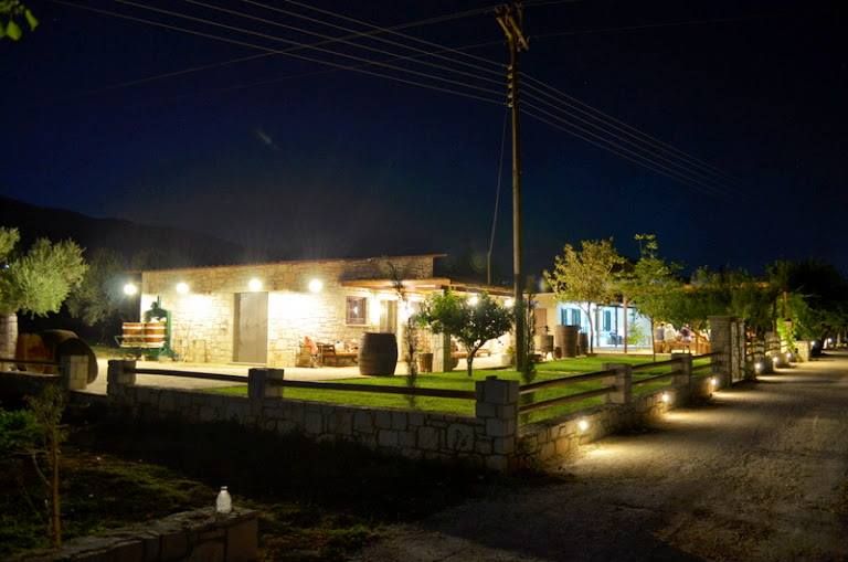 a corner of illuminated Klima Grampsa building by night with low stone fence
